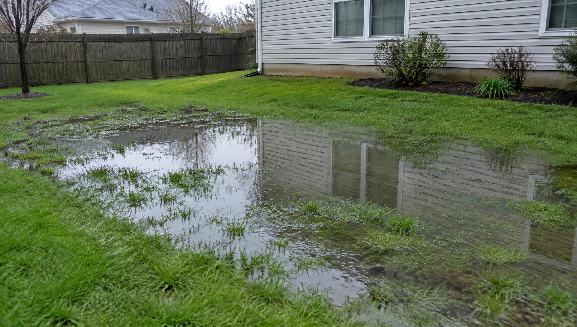 Standing water across a residential backyard lawn from poor drainage slope beside a house
